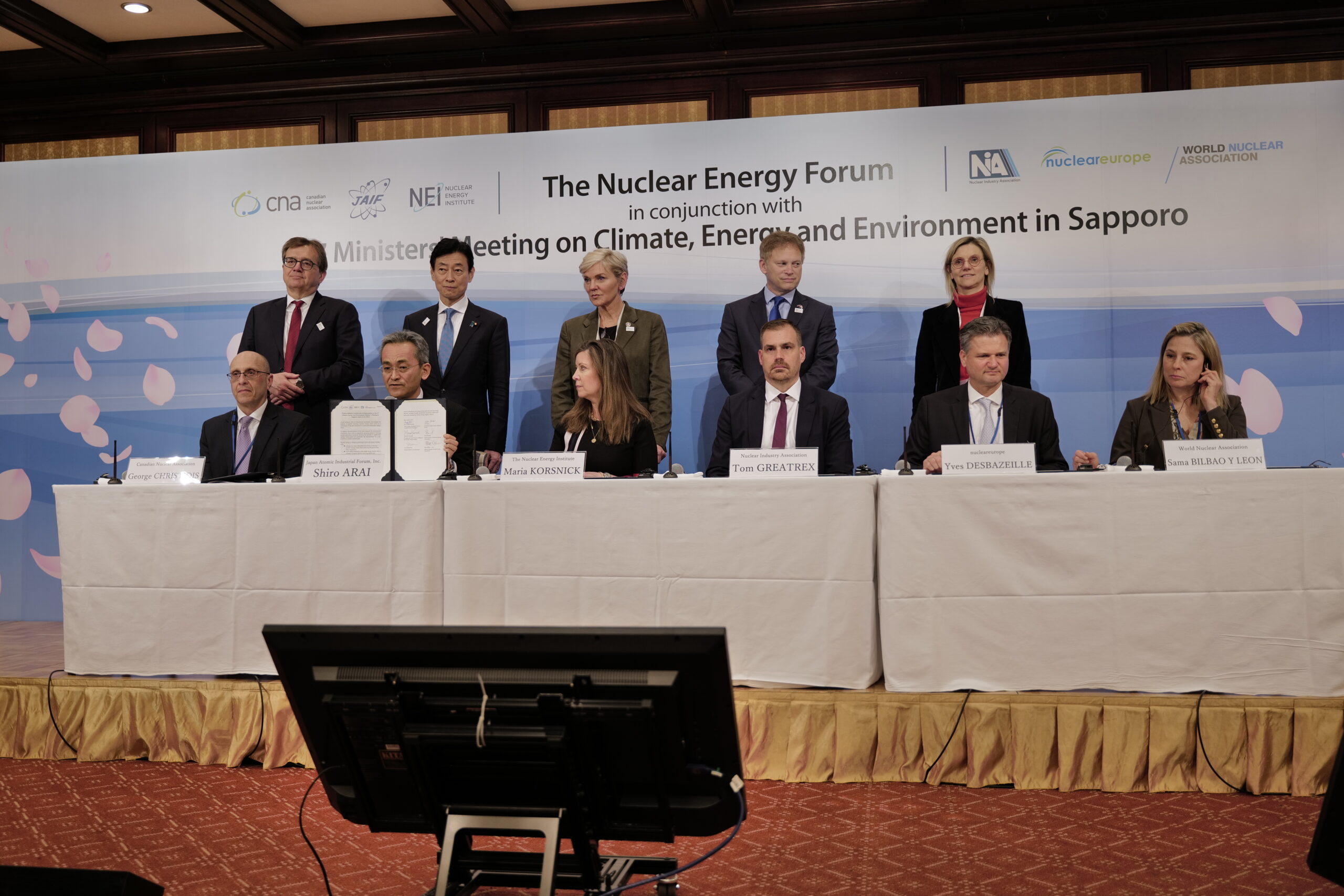 Speakers seated at a long table beneath a screen at the JAIF annual conference in Tokyo
