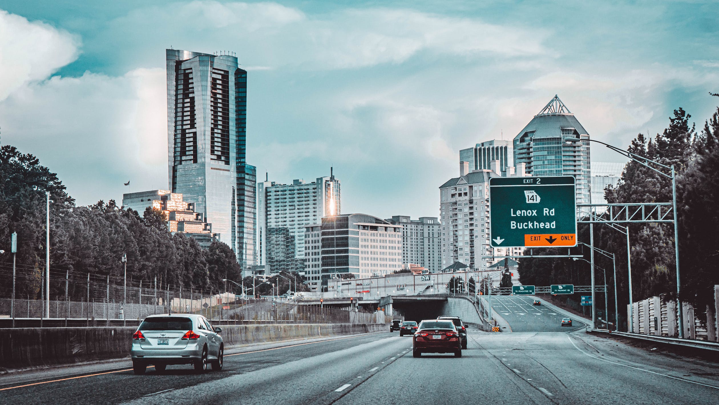 Traffic on an Atlanta freeway with the Buckhead skyline and a Lenox Road exit sign ahead