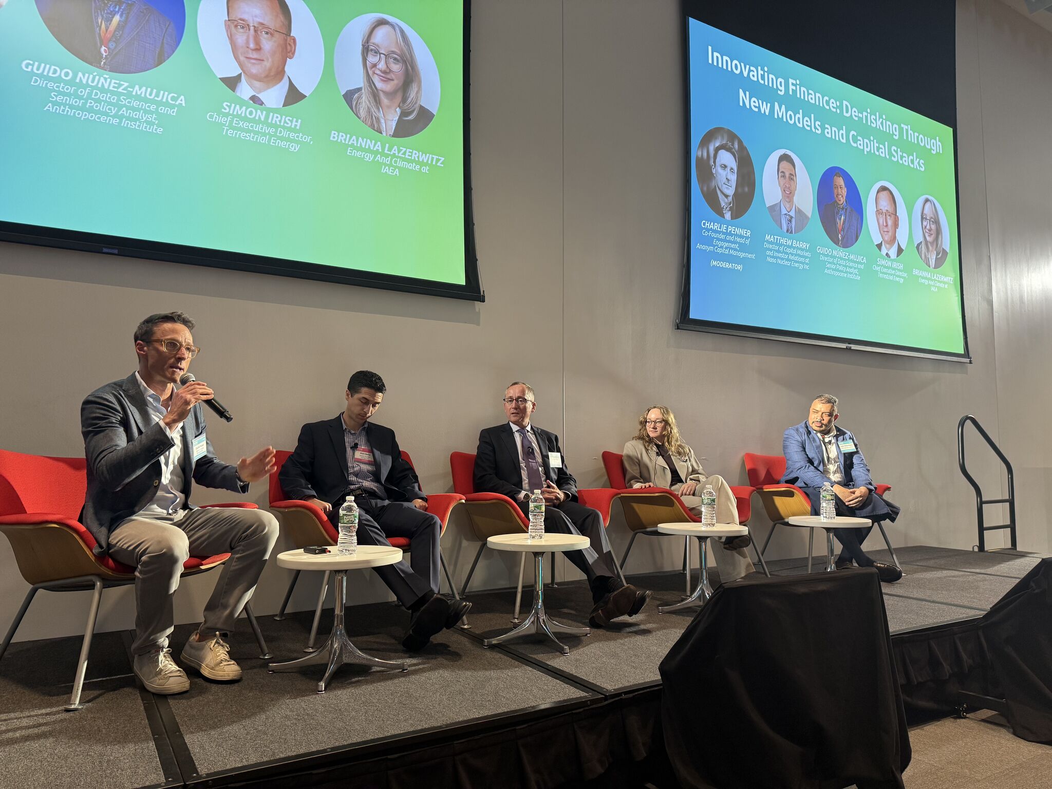 Panelists seated on stage in front of a screen showing the session speakers