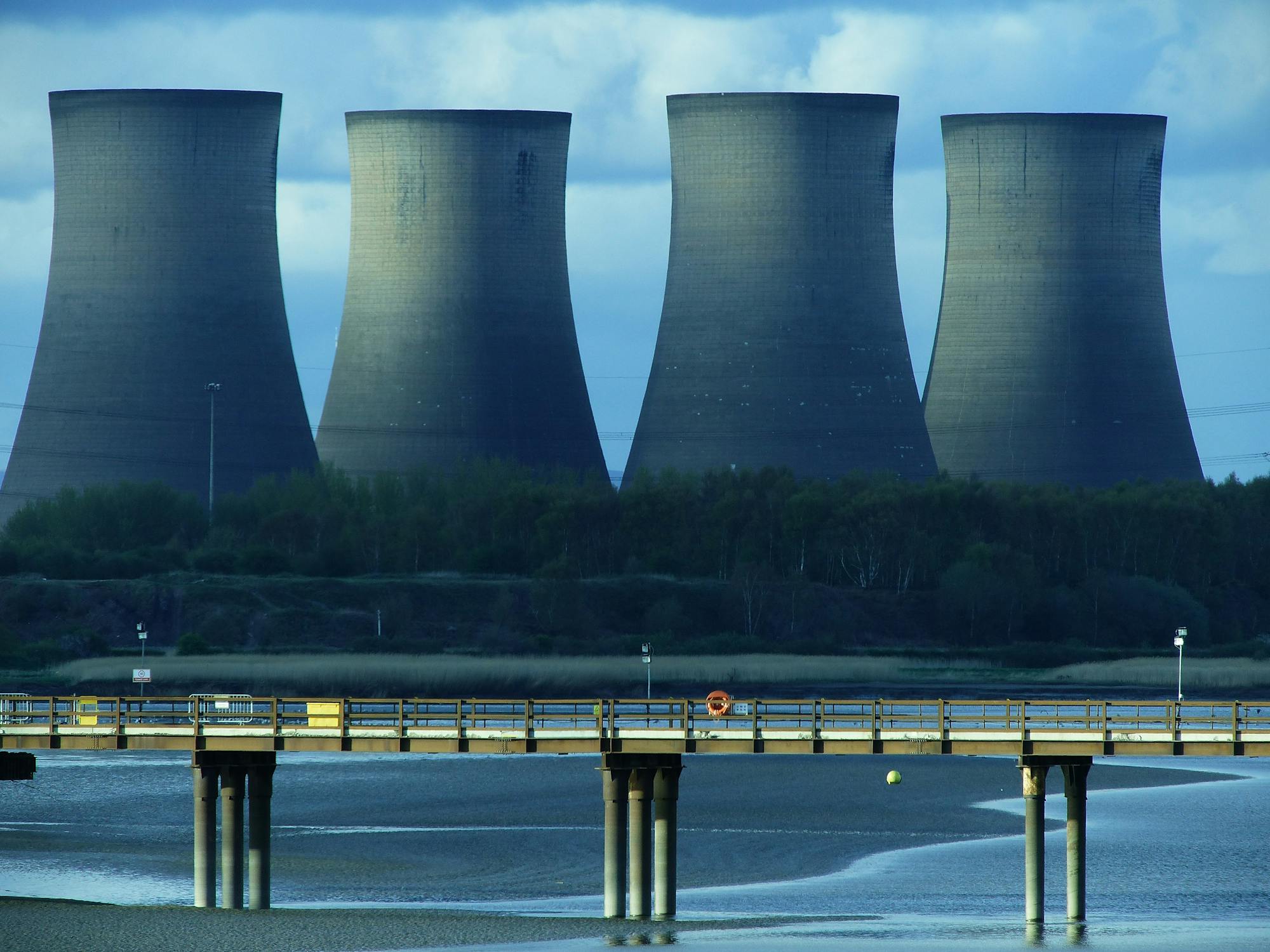 Four cooling towers of a power station rising beside calm water