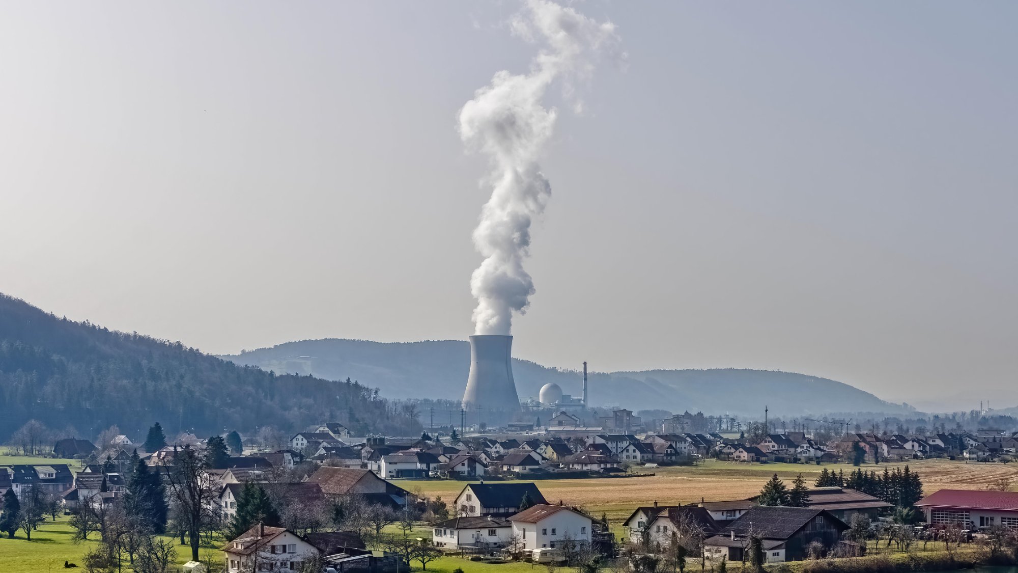 The Leibstadt nuclear power plant's cooling tower releasing a plume of steam above a village and farm fields in the Aargau countryside