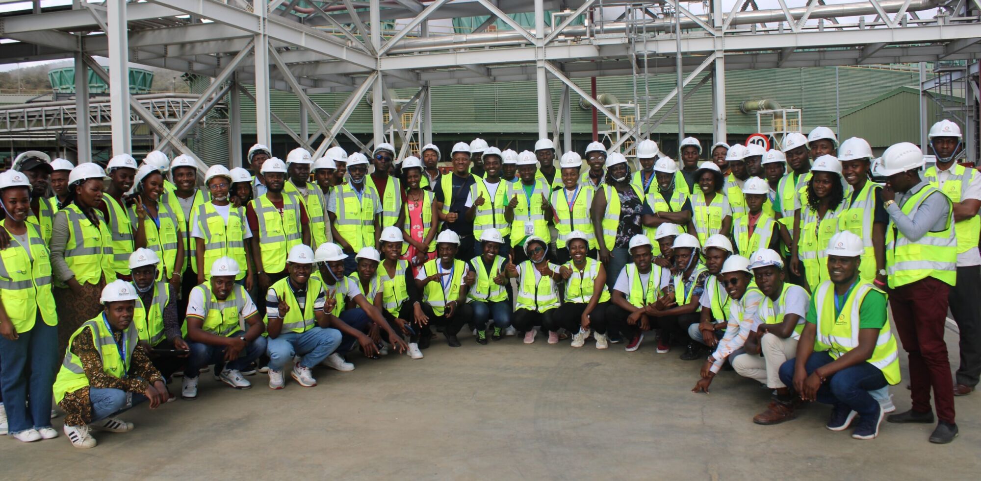 A large group of summit delegates in hard hats and high-visibility vests posed together inside a power plant